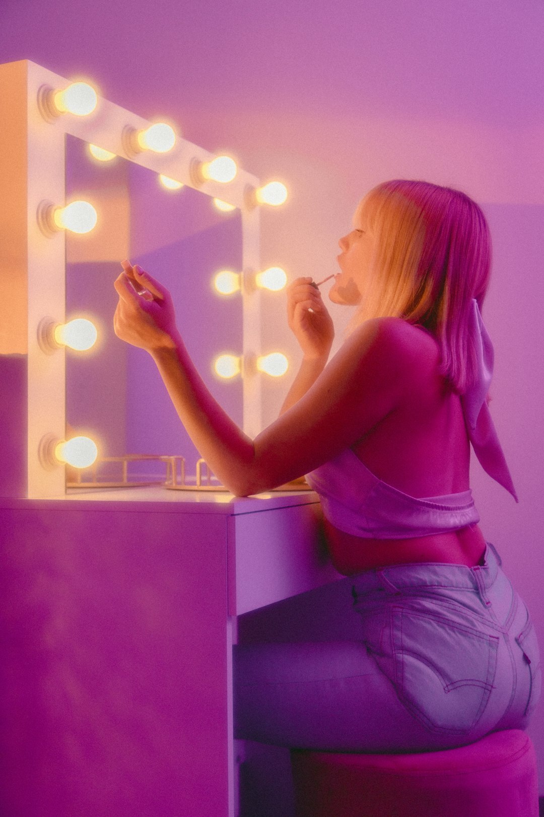 Woman looking into a mirror surrounded by dressing room lights