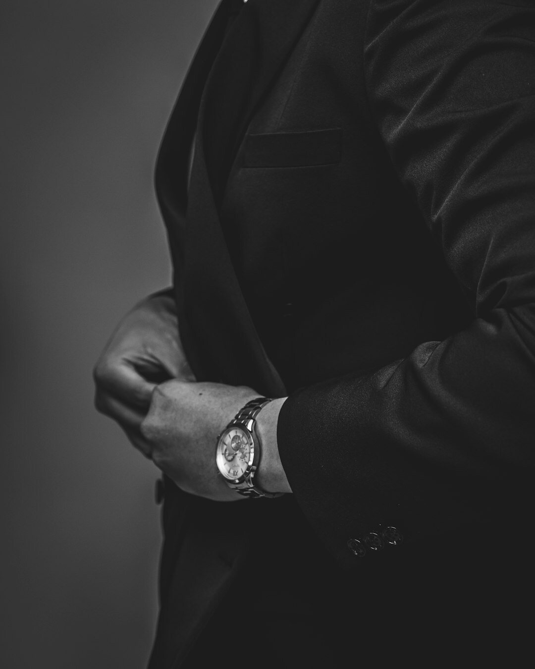 Man in a tailored charcoal suit adjusting his cufflink